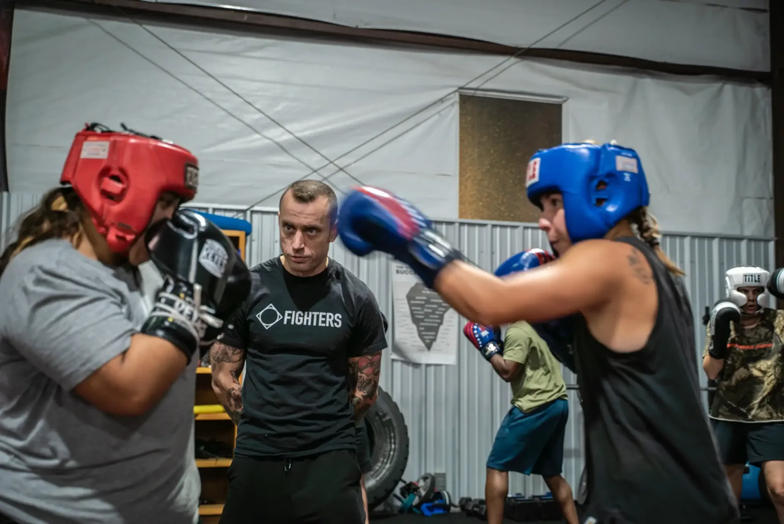 Two boxers sparring in headgear while a Fighters coach watches from the ropes